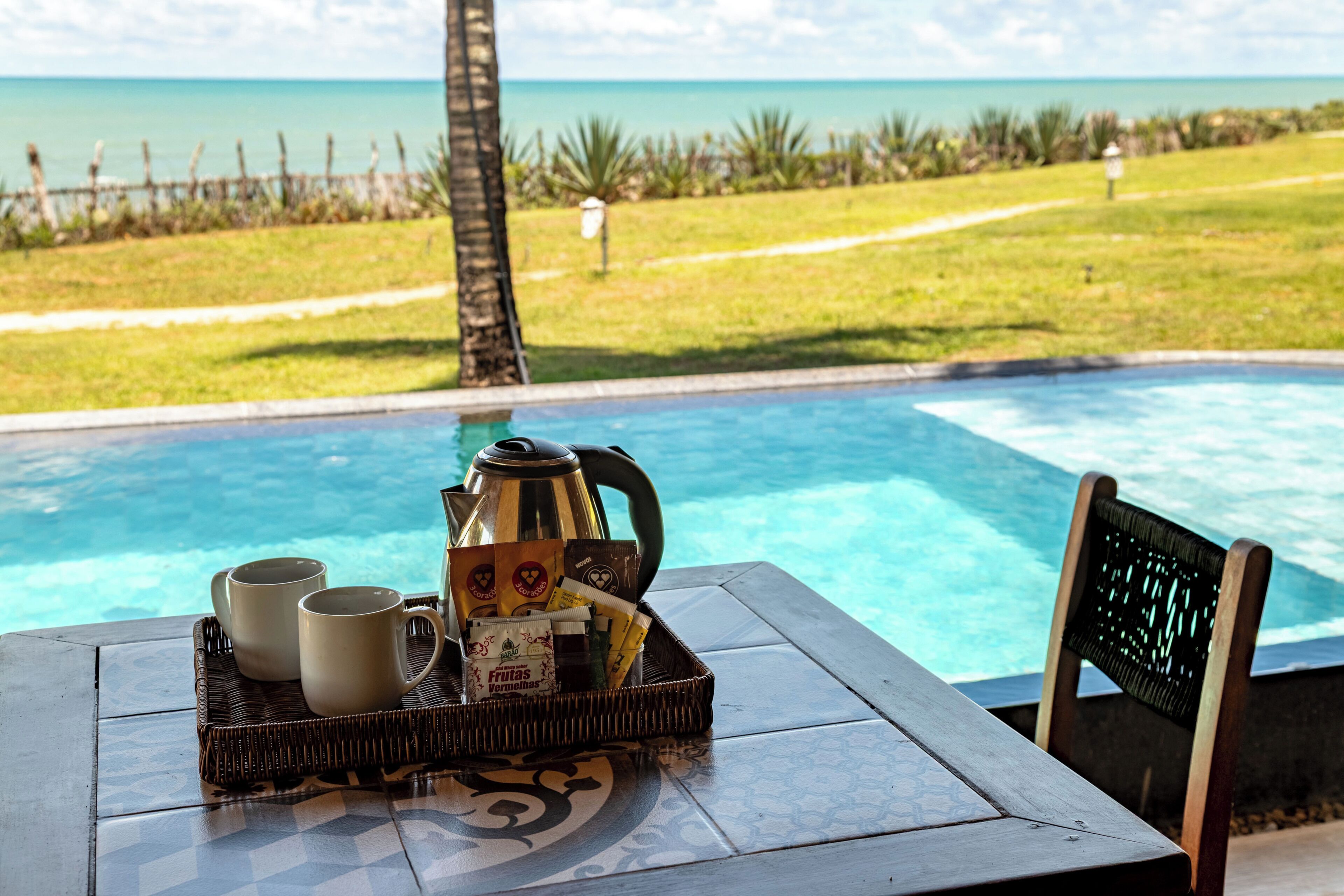 A poolside table with a tray of coffee cups, a coffee pot, and a basket of snacks.