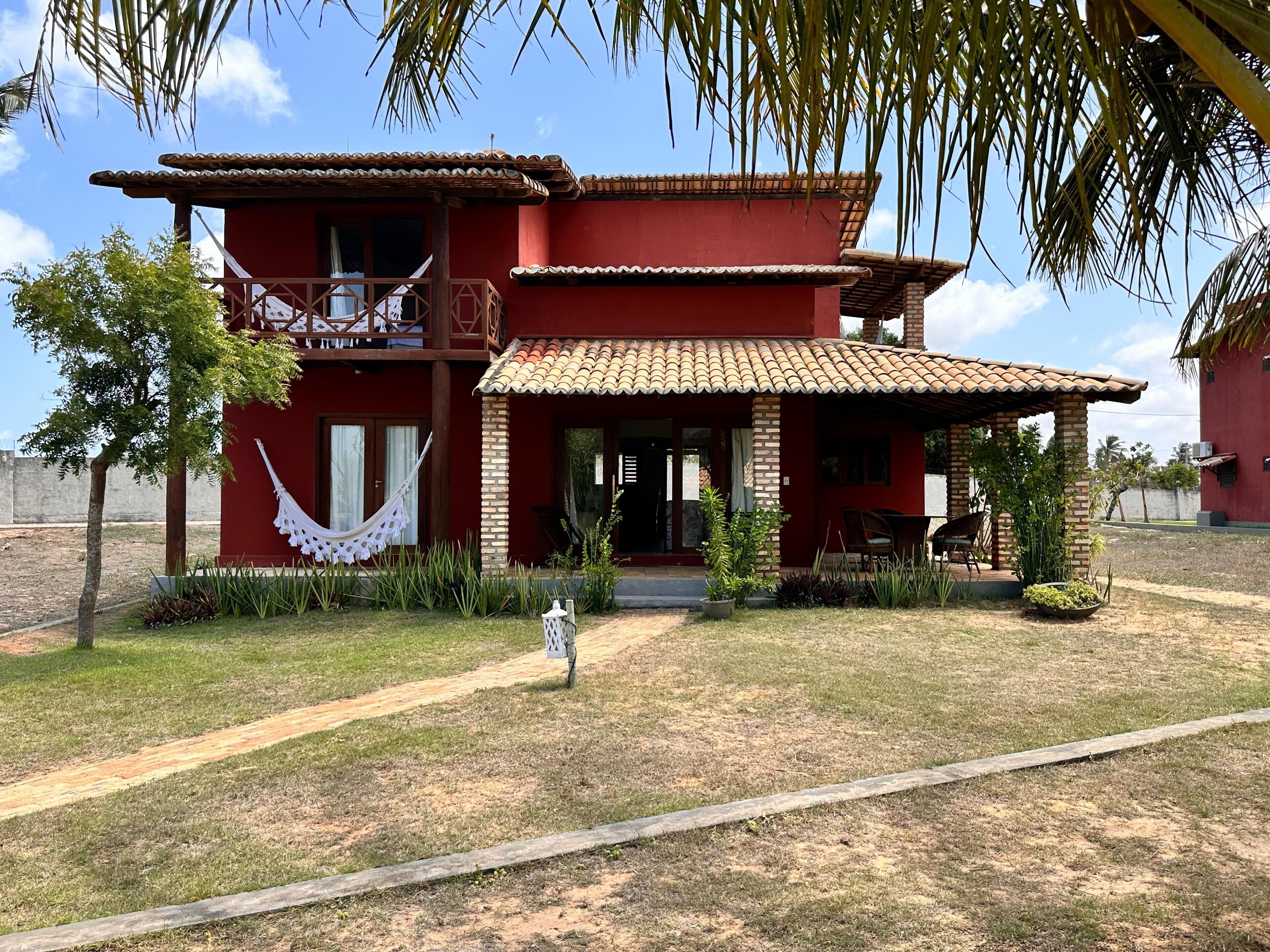 A two-story building with a red exterior and a tiled roof. There is a balcony on the upper floor and a covered porch with outdoor seating.