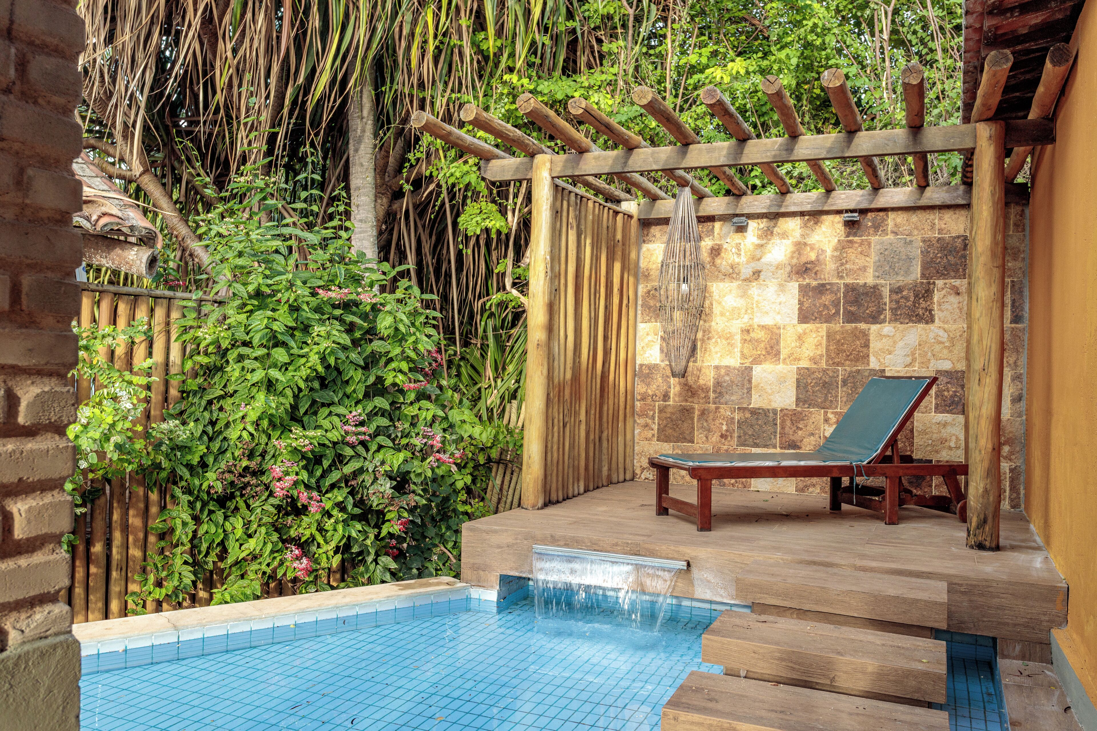 Piscina com deck de madeira, espreguiçadeira e parede de pedra.