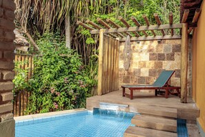 Una piscina con muelle de madera, una silla de descanso y un muro de piedra.