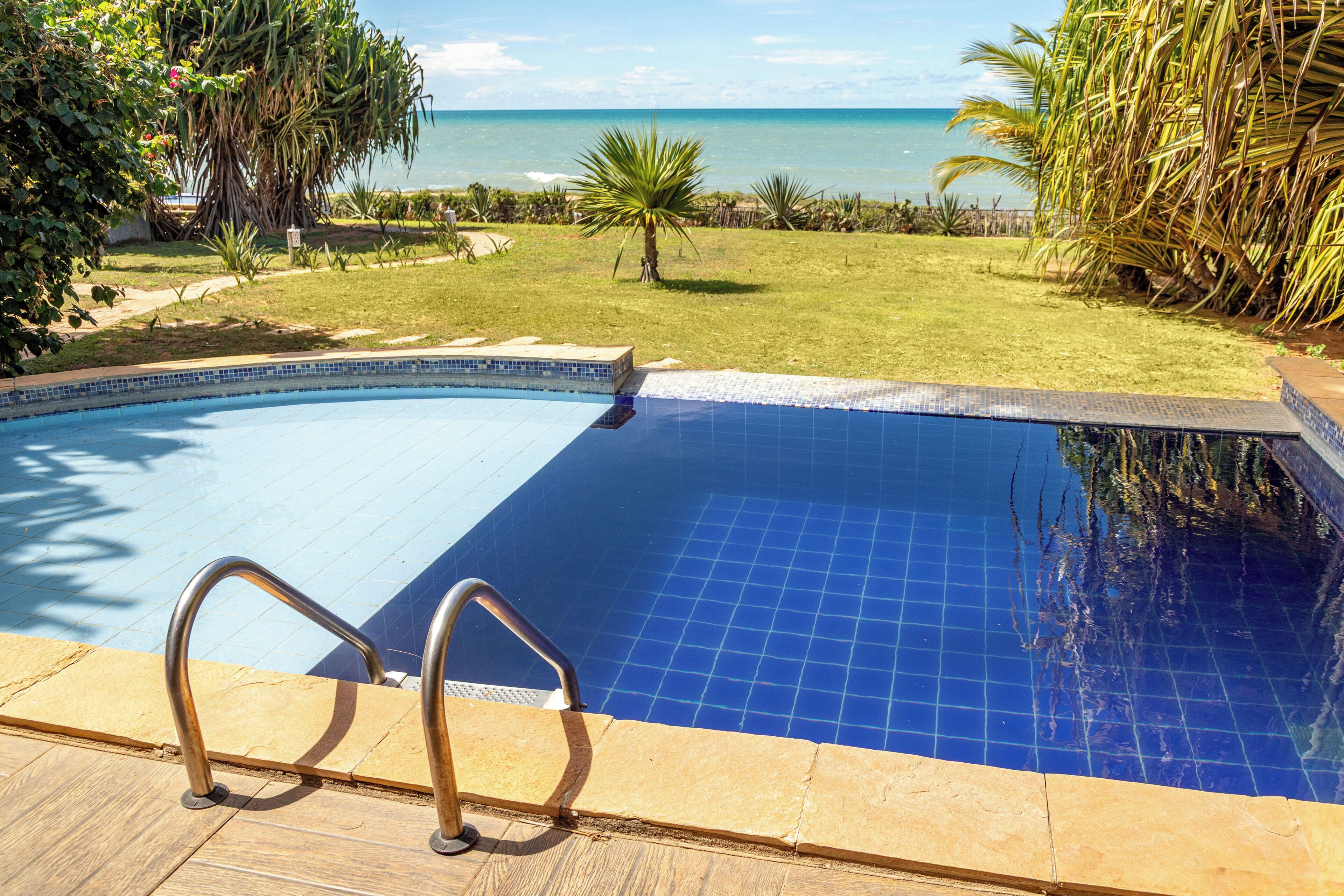 Una piscina con vista sull'oceano, circondata da piante tropicali e un cielo sereno.