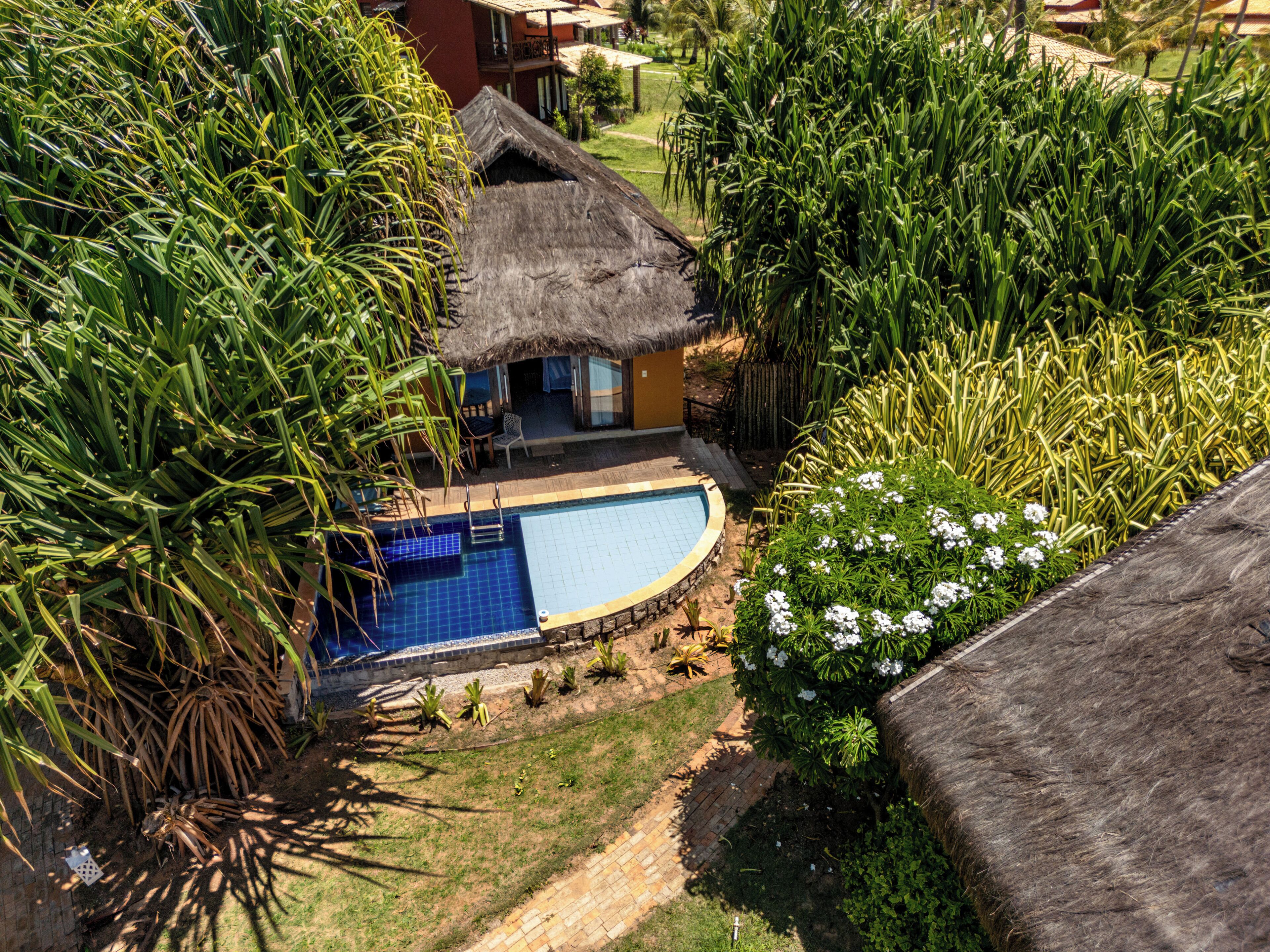 A resort with a swimming pool, a thatched-roof structure, and lush greenery.