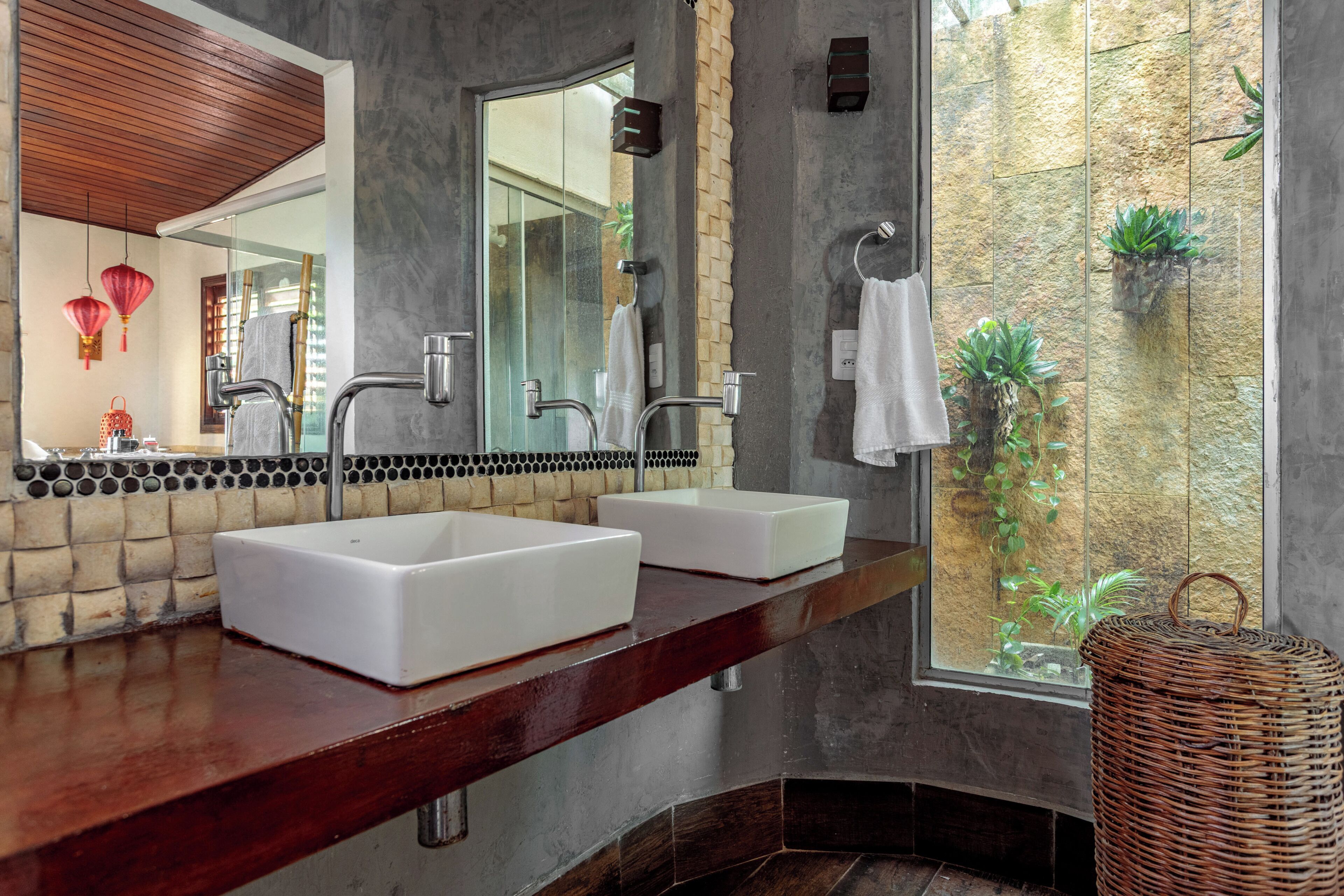 A bathroom with two sinks, a large mirror, and a view of a stone wall with plants.