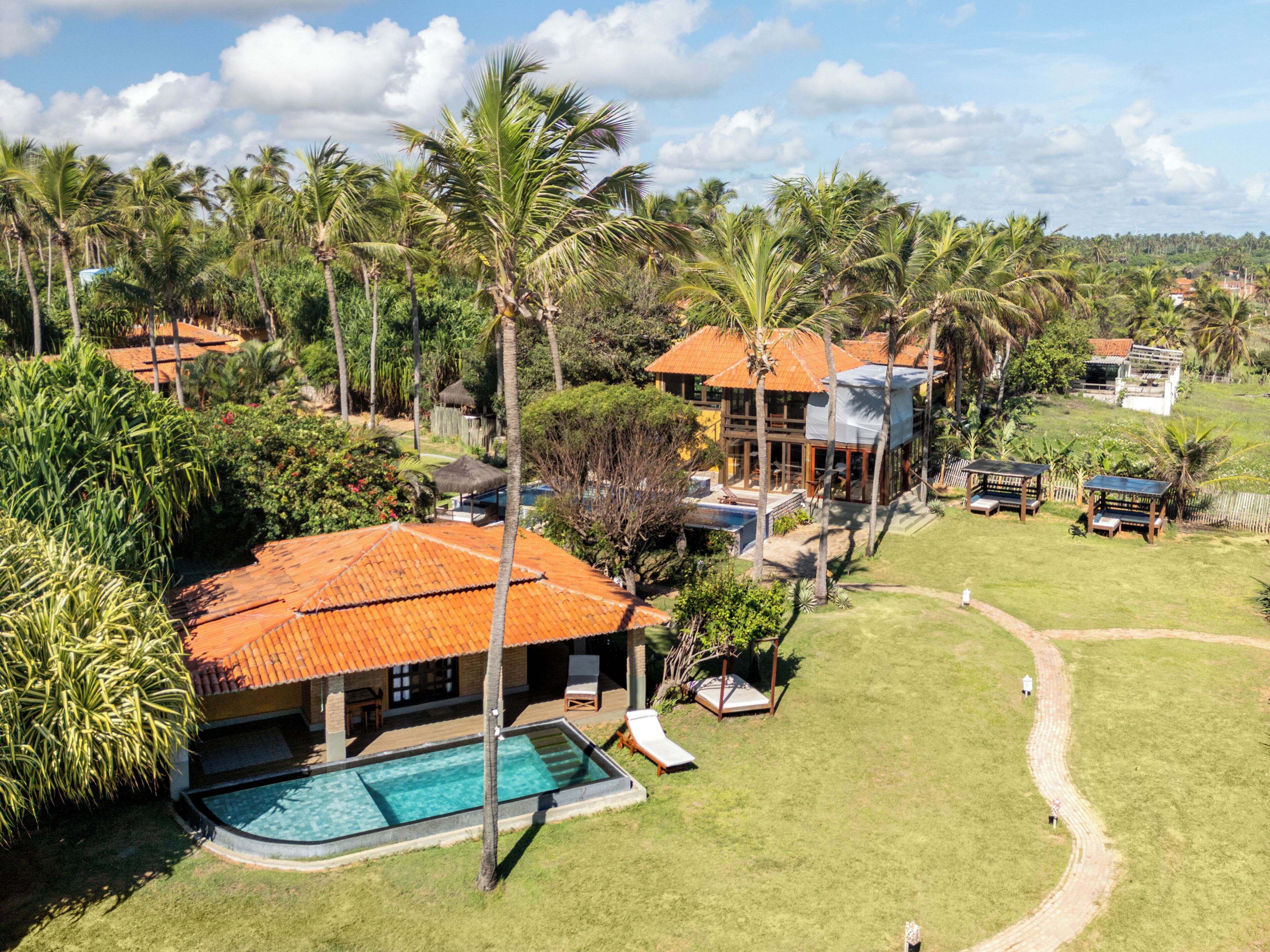 Une grande maison avec une piscine, entourée de palmiers et d’une pelouse bien entretenue.