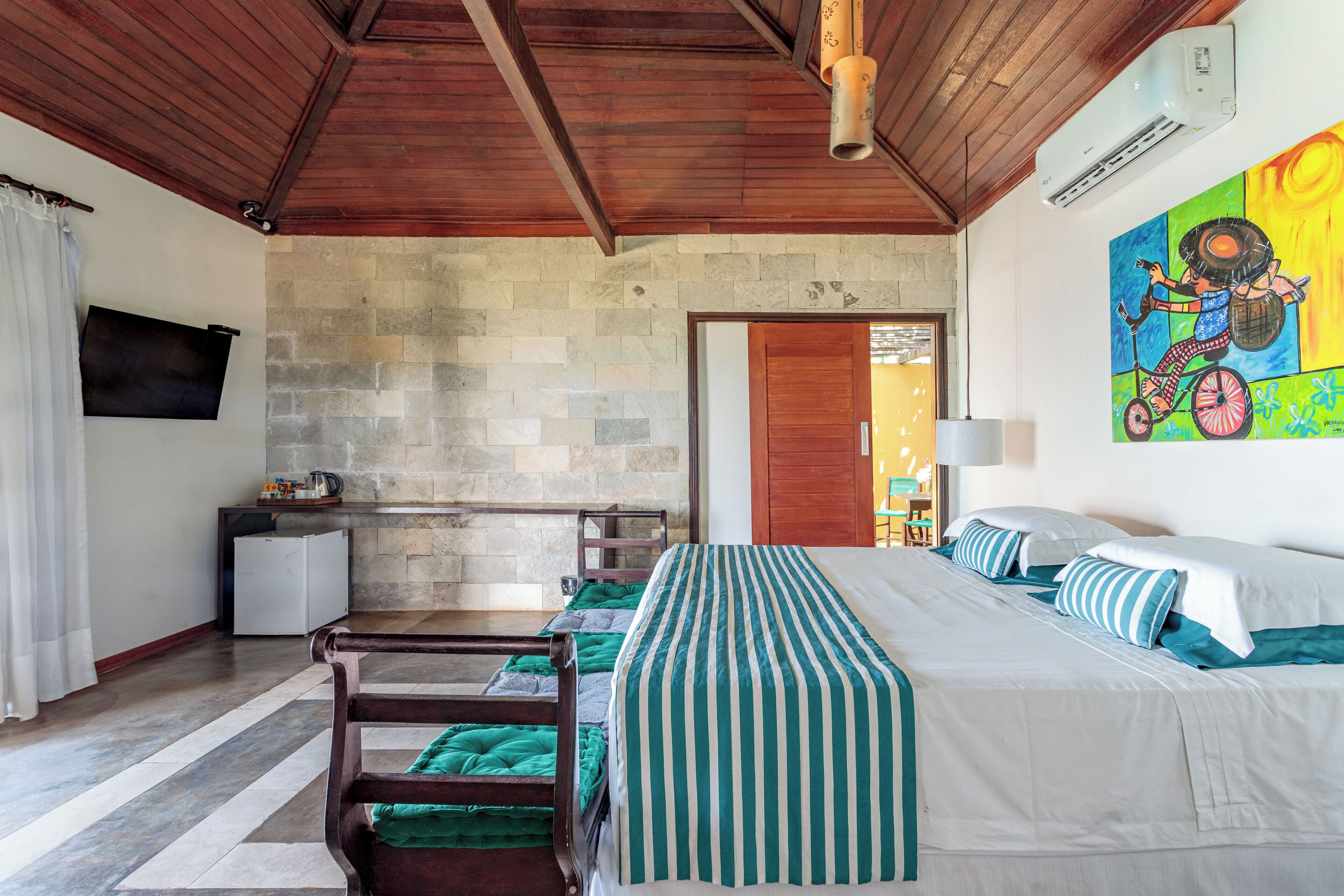 A room with a bed, a desk, a chair, a television, and a stone wall.