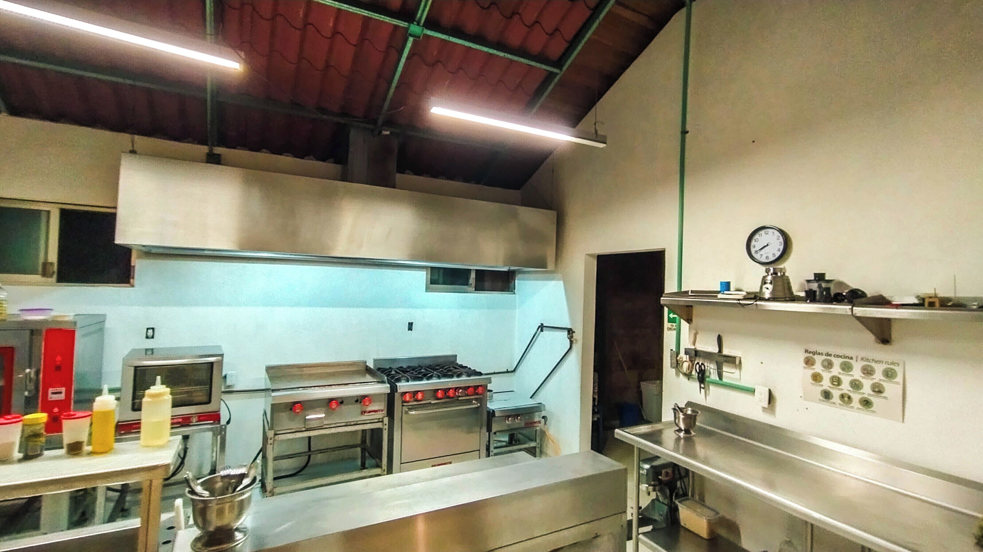Une cuisine professionnelle équipée d’appareils en acier inoxydable, notamment des fours et une cuisinière, et une horloge au mur.