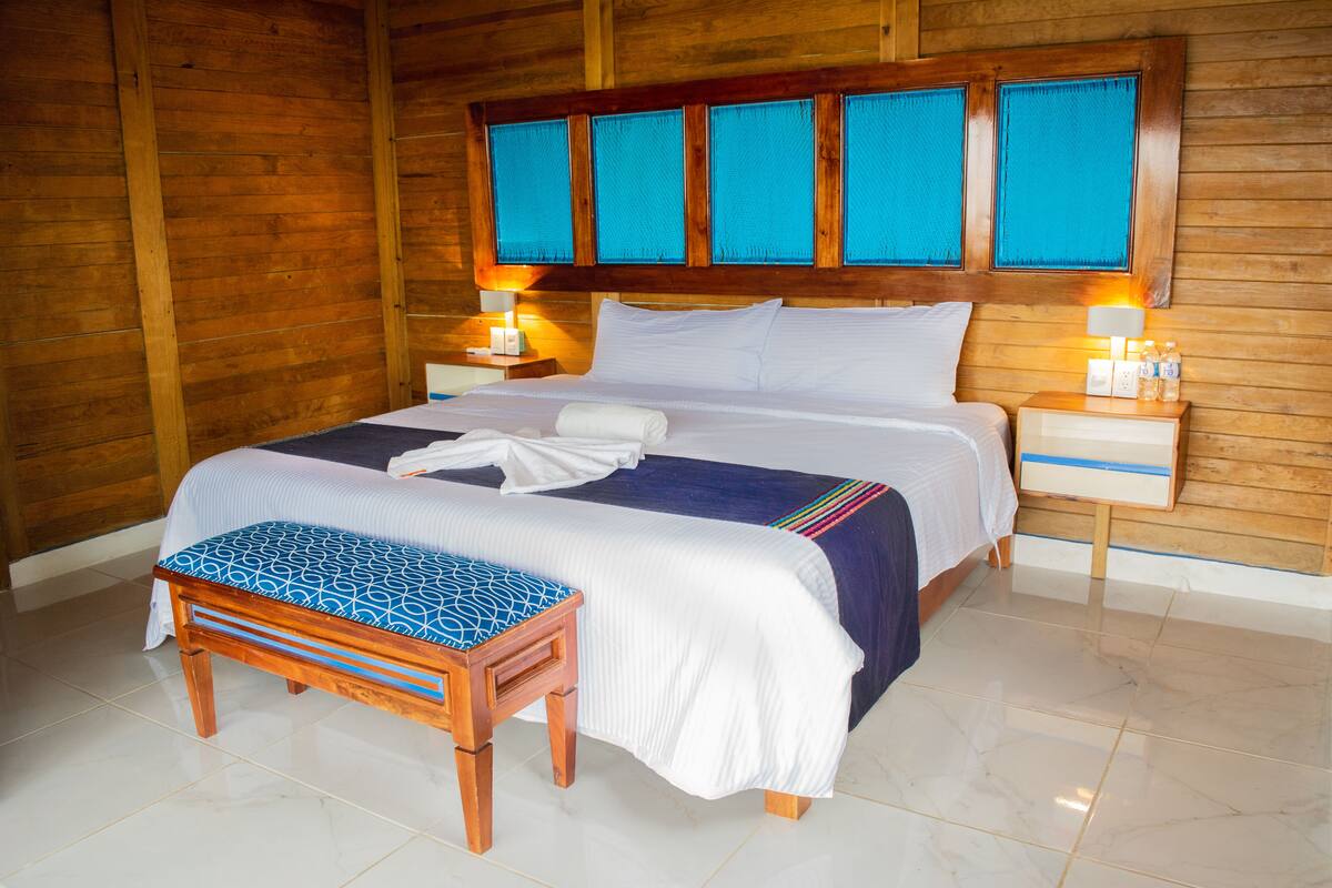 Una habitación con paneles de madera, una cama, mesitas de noche y un banco.