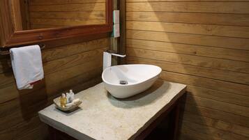 A wooden cabin-style bathroom with a white vessel sink, a wooden vanity, and a towel hanging on the wall.
