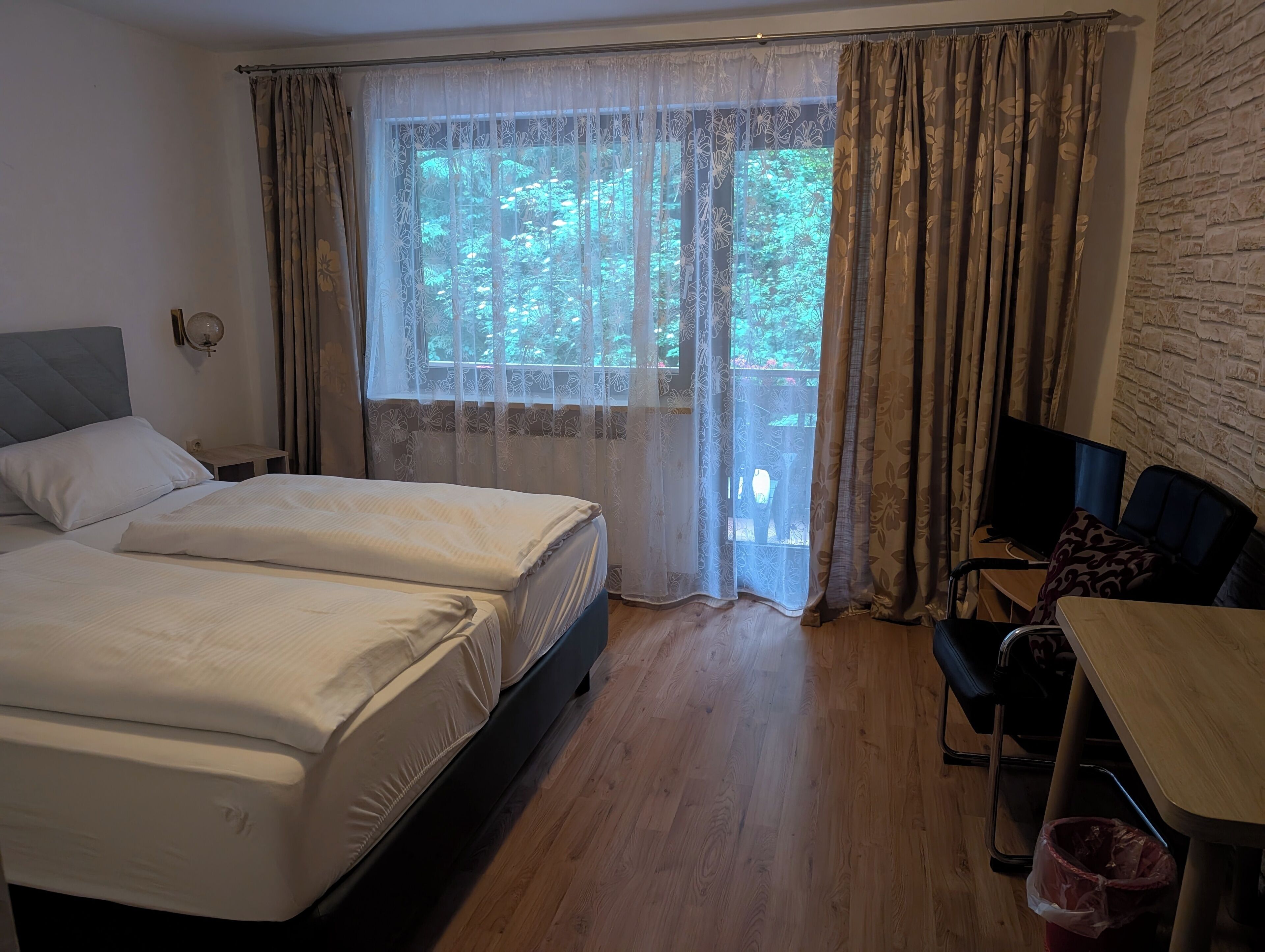 Et hotelværelse med to senge, et skrivebord, en stol og et fjernsyn.