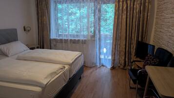 Et hotelværelse med to senge, et skrivebord, en stol og et fjernsyn.