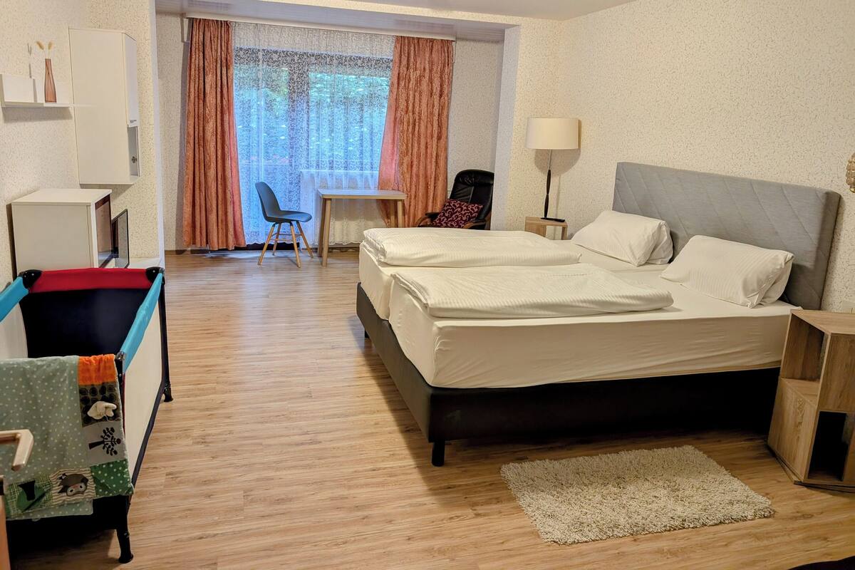 A hotel room with a bed, desk, chair, and a small table with a lamp.