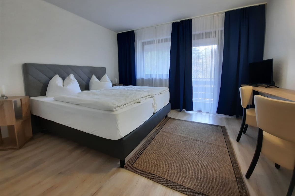 A hotel room with a bed, a desk, a chair, a television, and a window with curtains.