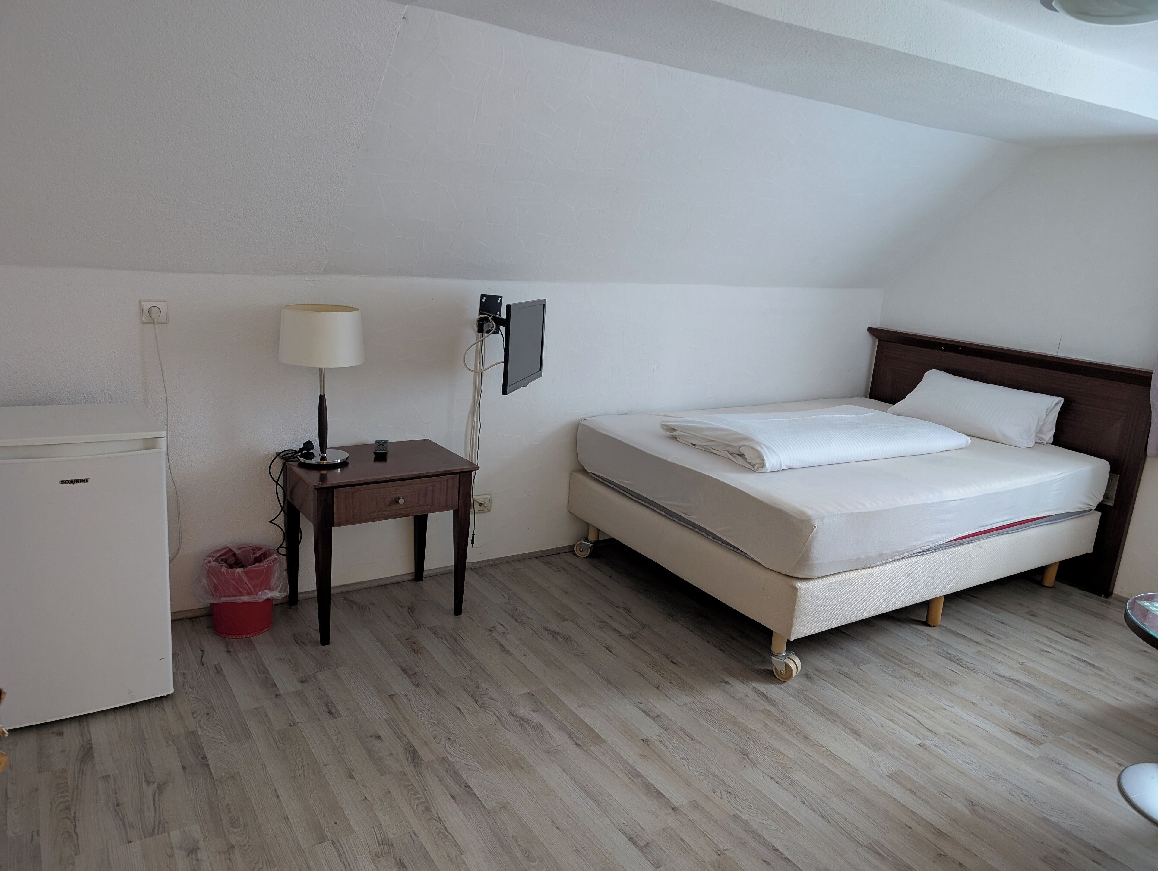 A small, clean room with a bed, a desk, a lamp, a TV, and a refrigerator.