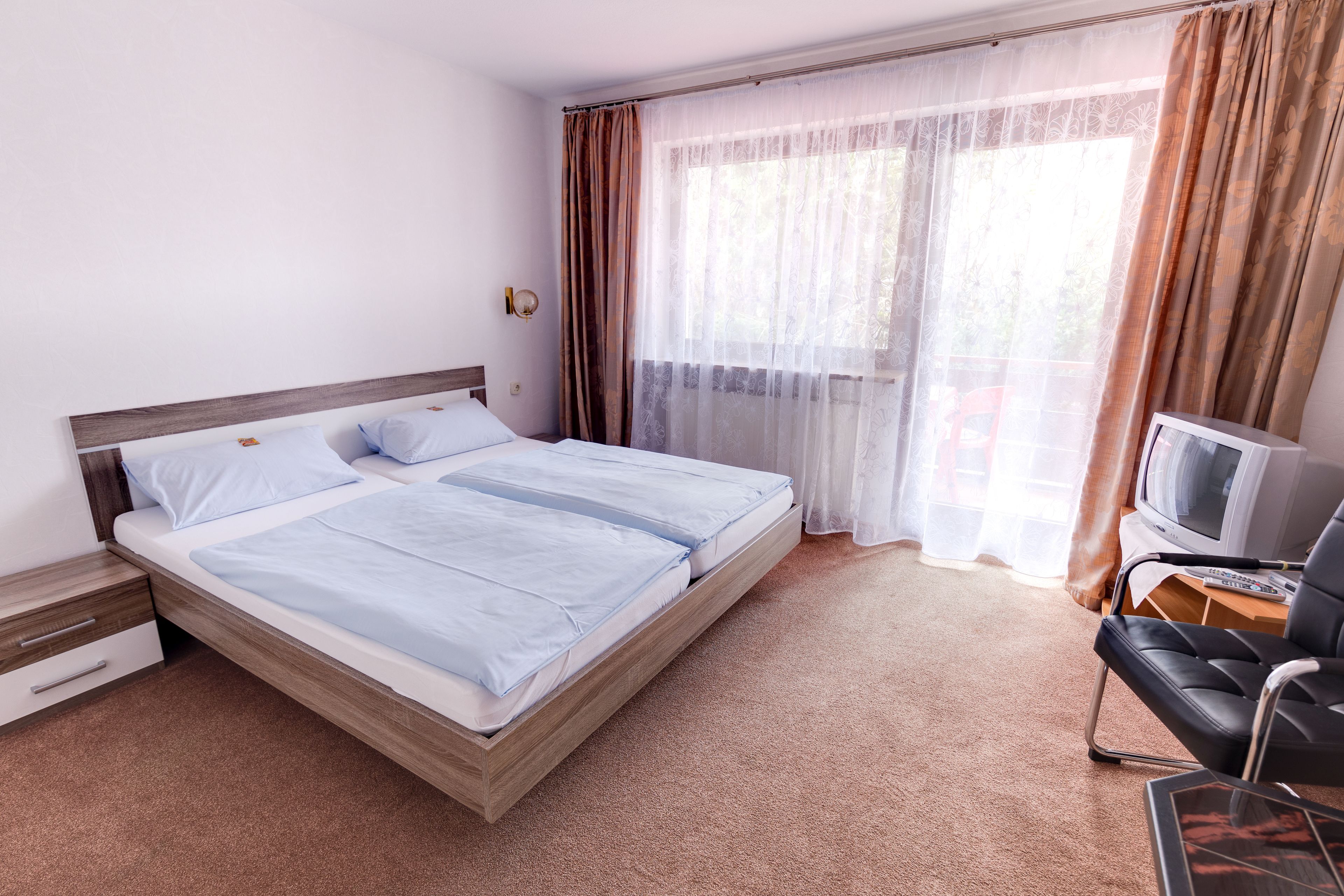 Une chambre d’hôtel comprenant un lit double avec une tête de lit en bois, une télévision et un bureau avec une chaise.