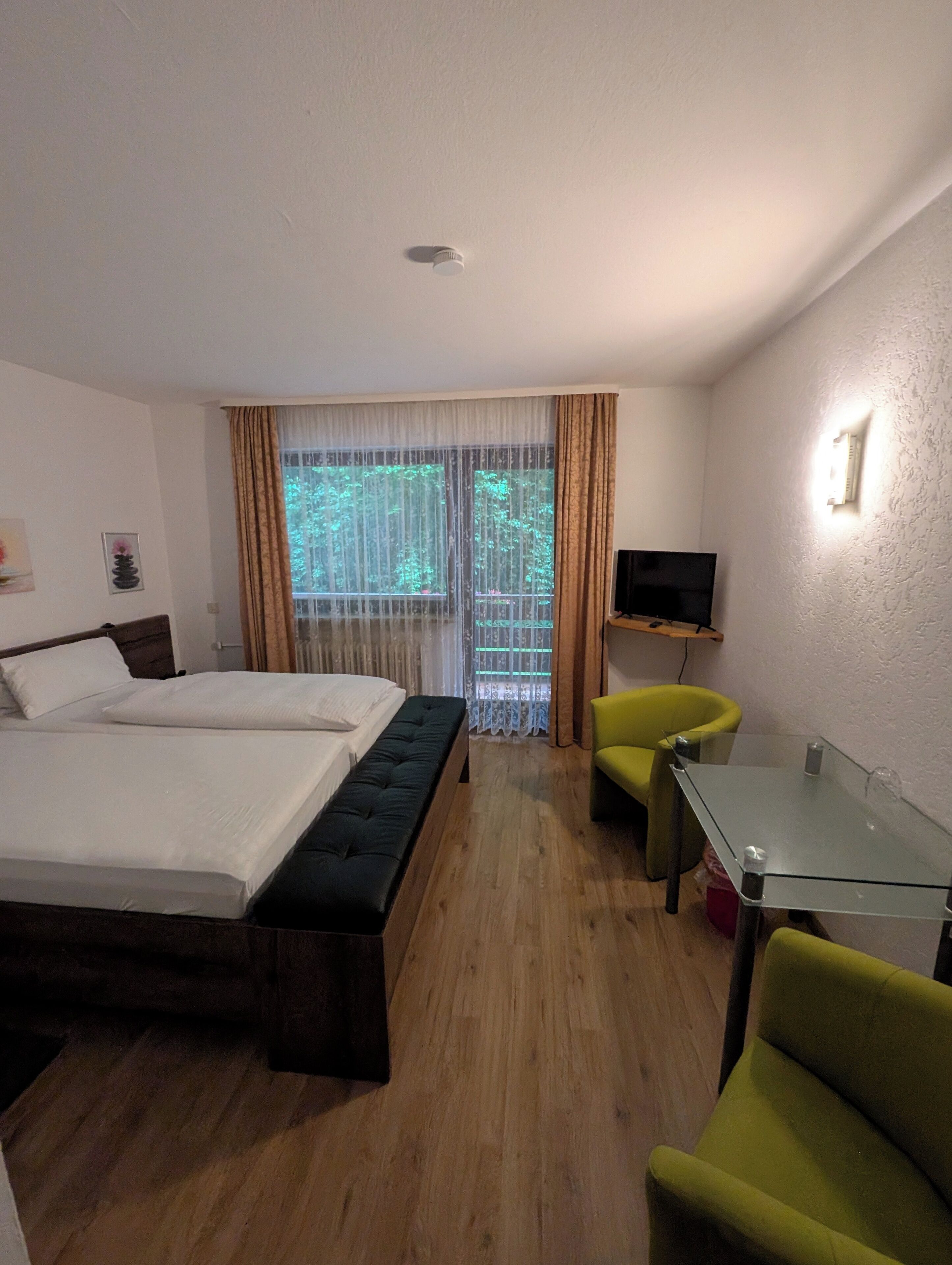 Una habitación de hotel con cama, una banca, un televisor y una mesa de vidrio.