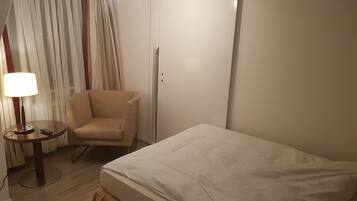 Ein Hotelzimmer mit Bett, Sessel, Lampe und Vorhang.