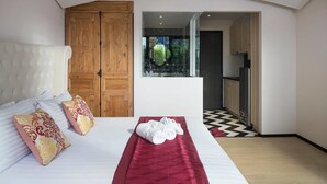 A hotel room with a large bed, wooden wardrobe, and a view through a window. - The Symphony Suites Pattaya (Pattaya)
