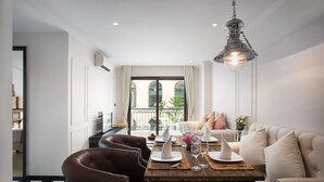 A dining area with a wooden table set for four, surrounded by leather chairs, a sofa, and a hanging light fixture. - The Symphony Suites Pattaya (Pattaya)