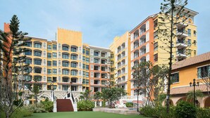 A multi-story hotel with balconies, a central courtyard with a statue, and a mix of yellow and orange building facades. - The Symphony Suites Pattaya (Pattaya)