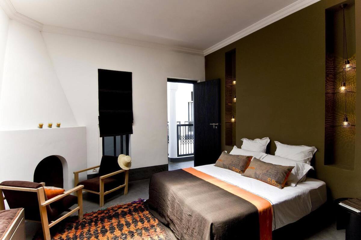 A bedroom with a bed, a chair, a small table, and a view of the outside.