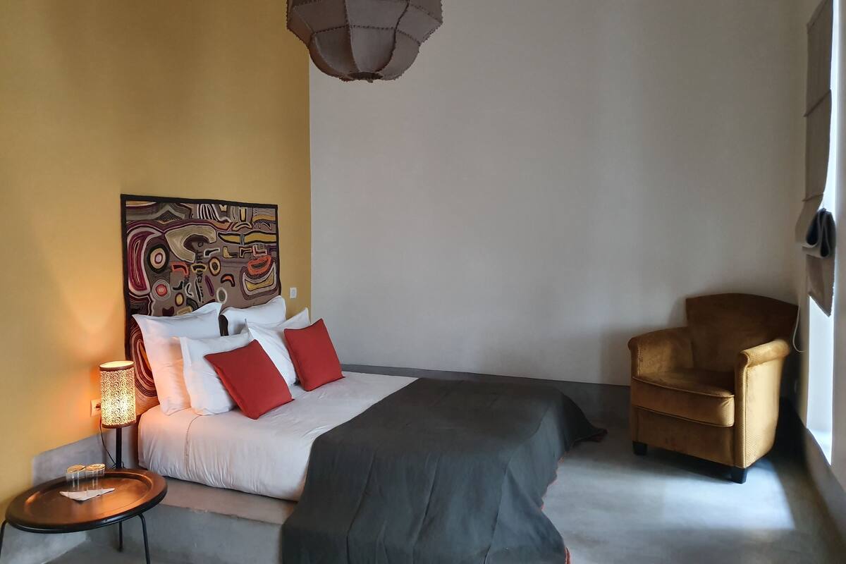 A bedroom with a bed, a chair, a lamp, and a painting on the wall.