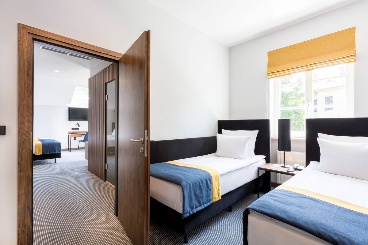 A hotel room with two beds, a desk, and a window with blinds.