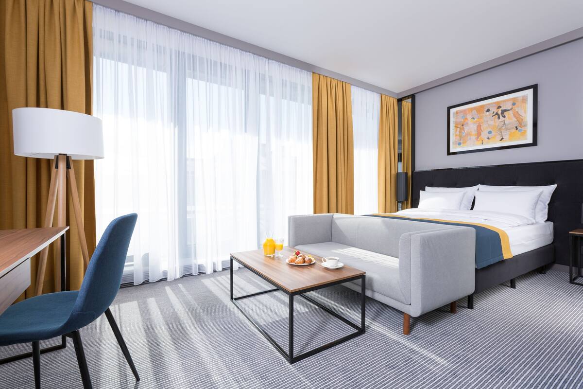 A hotel room with a bed, a sofa, a desk, and a coffee table.