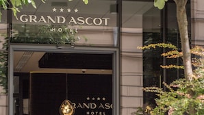 Entrada do Grand Ascott Hotel, com um balcão de recepção e um homem em pé atrás dele.