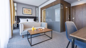 Quarto de hotel moderno com cama, sofá, mesa de jantar e preparação para o pequeno-almoço.