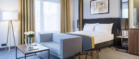 A hotel room with a bed, a desk, a chair, a lamp, and a painting on the wall.