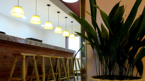 A bar area with wooden stools and hanging pendant lights. - 25 Four Seasons Youth Hostel (Qingdao)
