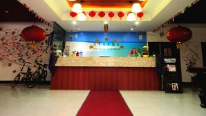 A reception area with a red carpet, a counter, and a wall with a scenic mural. - 25 Four Seasons Youth Hostel (Qingdao)