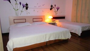 A hotel room with two single beds, a wooden floor, a nightstand with a lamp, and wall decorations including flowers and a lantern. - 25 Four Seasons Youth Hostel (Qingdao)