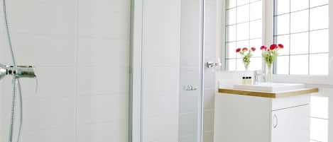 A modern bathroom with a glass-enclosed shower, a white vanity with a mirror, and a window providing natural light.