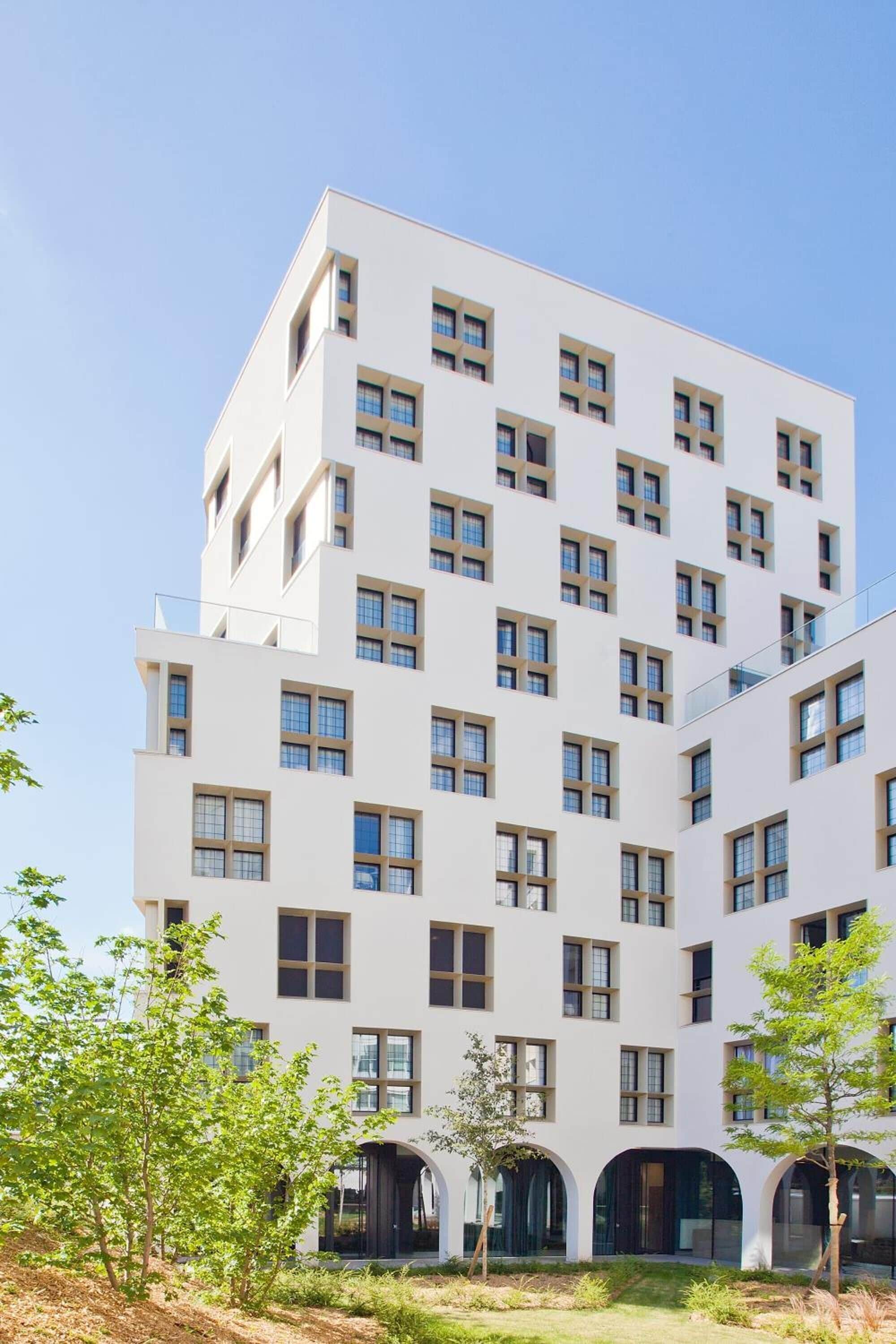 Un immeuble moderne à plusieurs étages, doté d’une façade blanche et de nombreuses fenêtres.