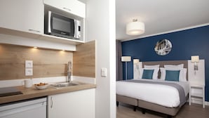 A modern hotel room with a kitchenette, a bed with a headboard, bedside tables, and a wall-mounted picture. - Residhome Paris Gare de Lyon - Jacqueline De Romilly (Paris)