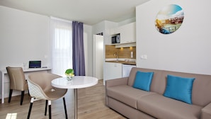A modern living room with a beige sofa, a round table, and a dining area with chairs. - Residhome Paris Gare de Lyon - Jacqueline De Romilly (Paris)