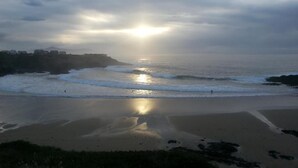 Una playa con un atardecer sobre el océano, una montaña distante y un cielo nublado.