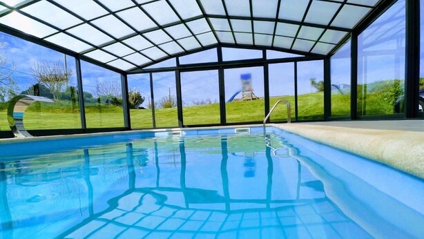 Una piscina con techo de cristal, rodeada de césped y un cielo despejado.
