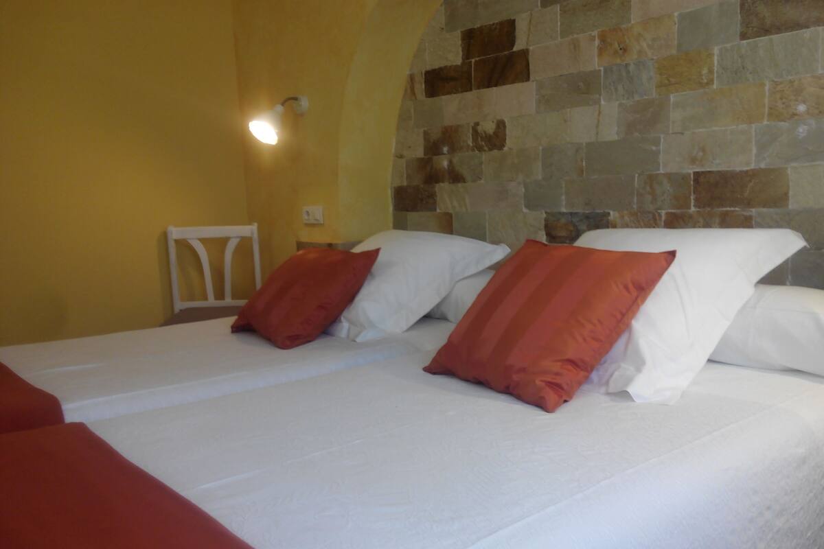 Ein Doppelbett mit weißen und orangefarbenen Kissen, einem weißen Kopfteil und einer Steinwand im Hintergrund.