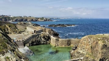 Una zona costanera amb un talús rocos, mar d'un blau clar i un petit moll.