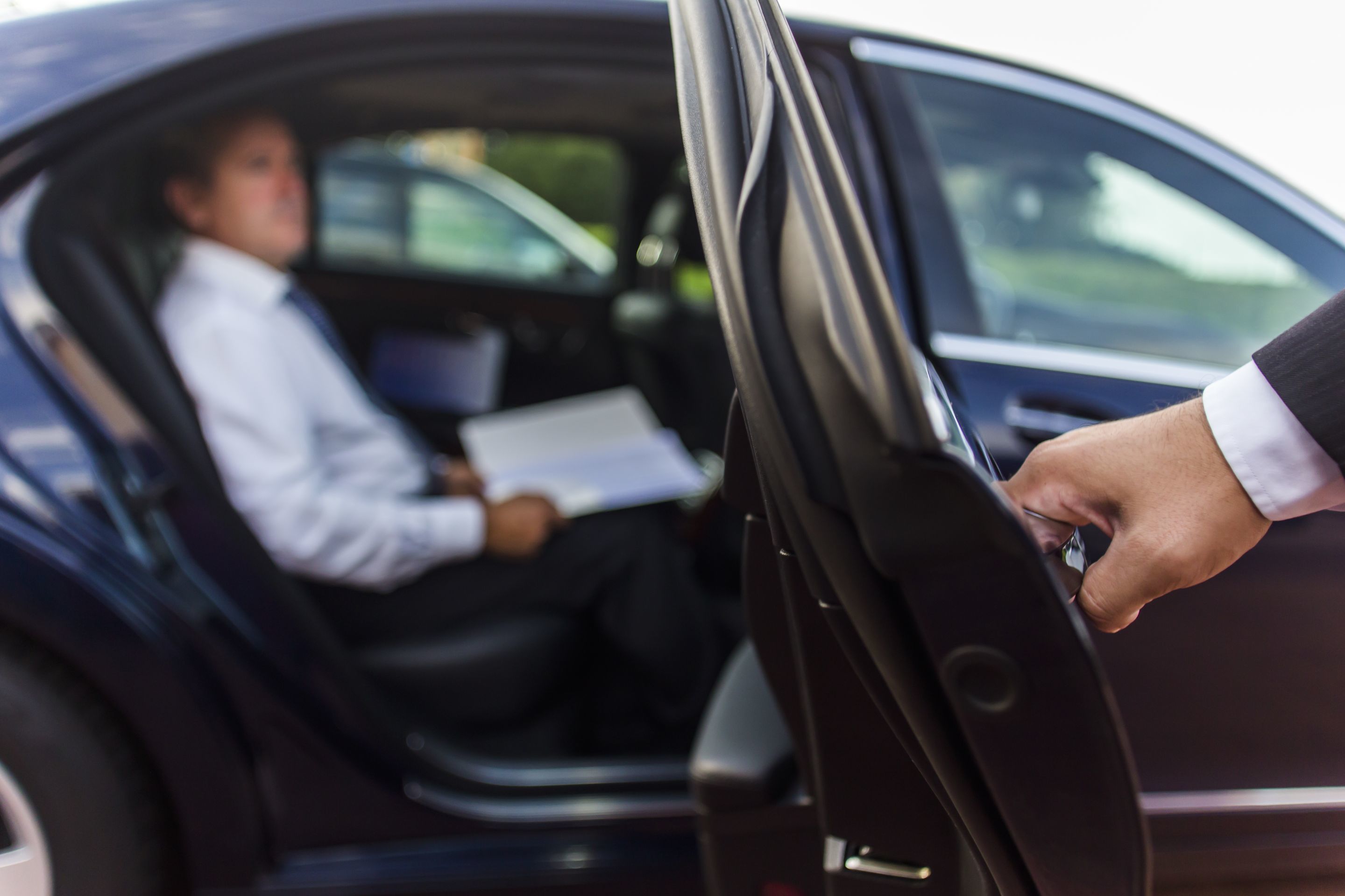 Una persona entregando un documento a un conductor a través de la puerta del auto.