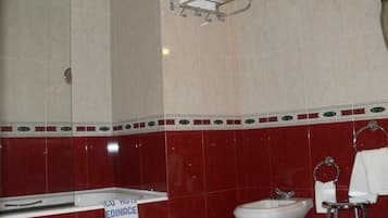 Un baño con bañera, lavabo y bidé. Hay un perchero sobre el lavabo y una toalla colgada.