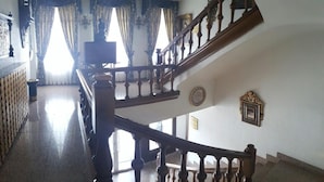 A grand staircase with ornate railings and a polished floor, leading to a landing with a view of the outside. - Nico Hotel (Medinaceli)