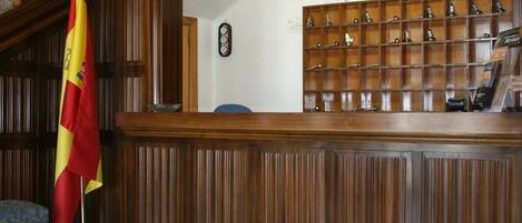 A reception area with a wooden paneled wall, a flag, a clock, and a display of various items on shelves.