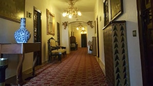 A hallway with patterned carpet, a chandelier, and a dining area with chairs and a table. - Nico Hotel (Medinaceli)