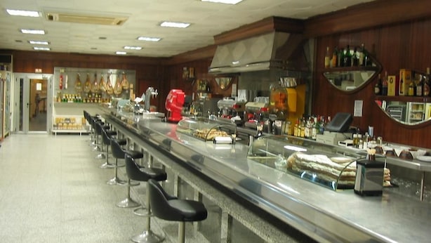 A bar area with a long counter, multiple stools, and a variety of bottles and glasses. - Nico Hotel (Medinaceli)