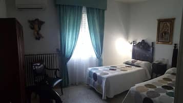 A bedroom with two beds, a chair, a radiator, and a window with curtains.