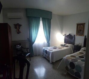 A bedroom with two beds, a chair, a radiator, and a window with curtains. - Nico Hotel (Medinaceli)