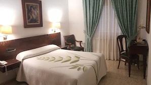 A hotel room with a bed, two chairs, a desk, a lamp, and a painting on the wall. - Nico Hotel (Medinaceli)